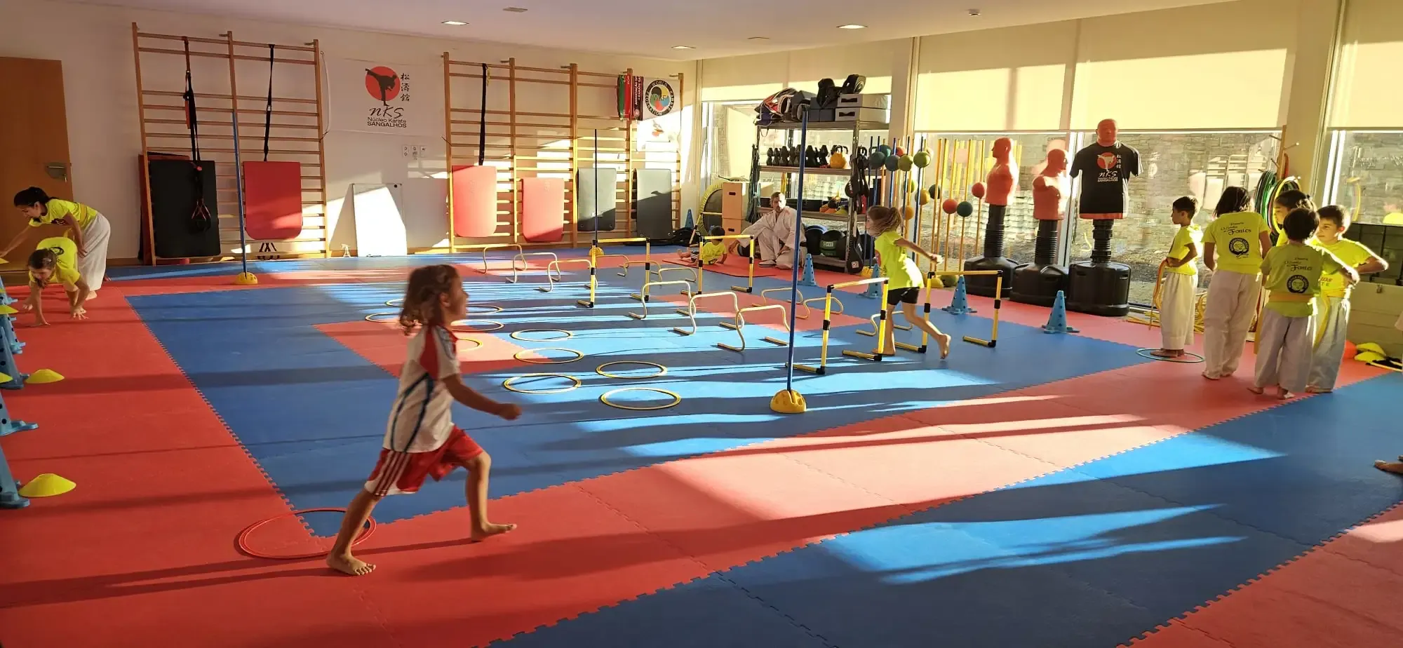 Crianças num circuito de agilidade com barreiras e arcos no dojo