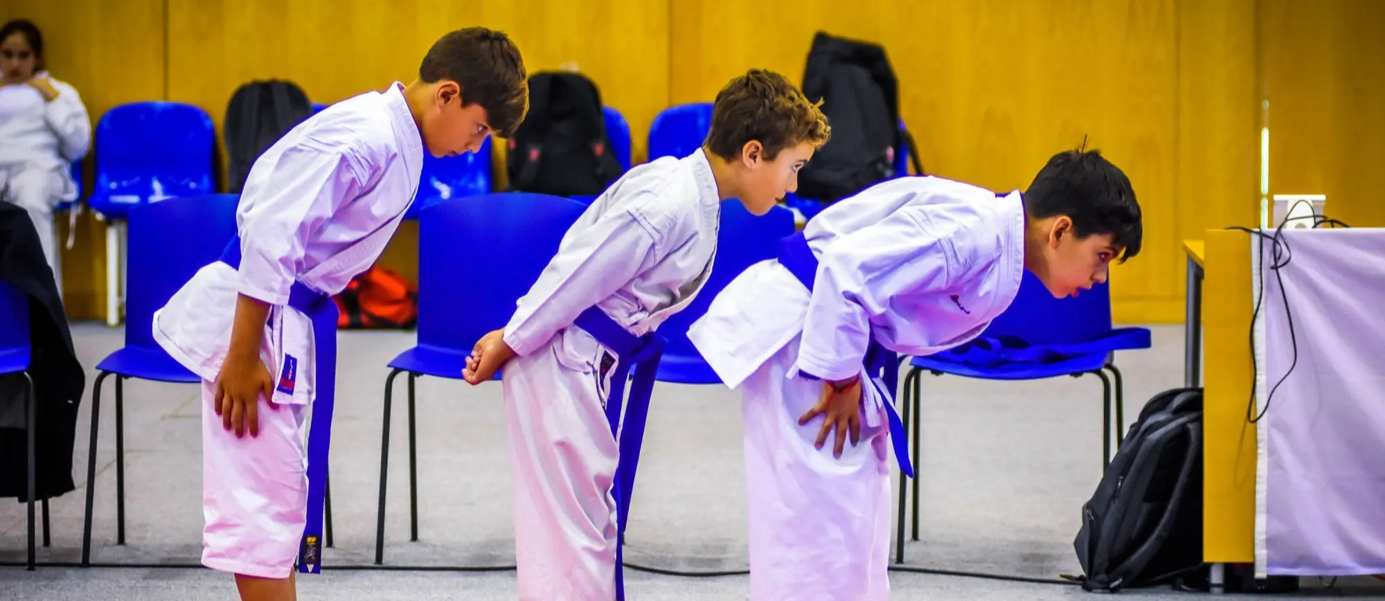 Três jovens atletas de cinto azul fazem a saudação numa competição